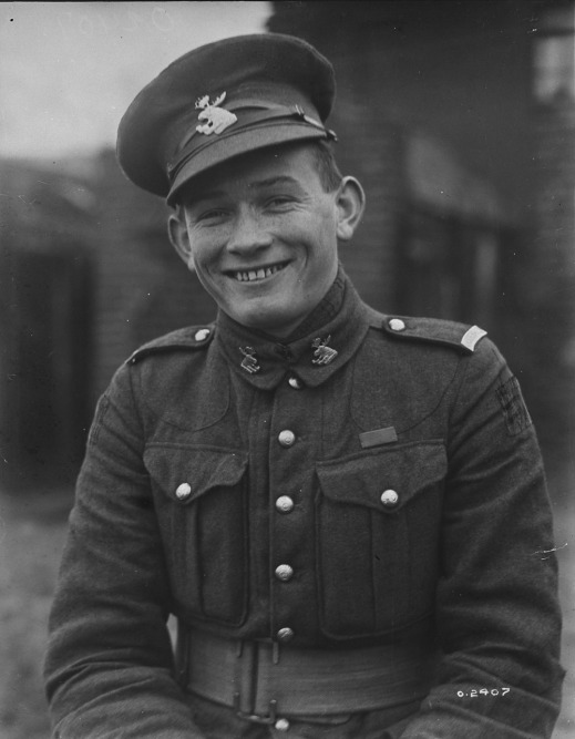 A black-and-white photograph of a smiling young man in uniform with his cap slightly askew.